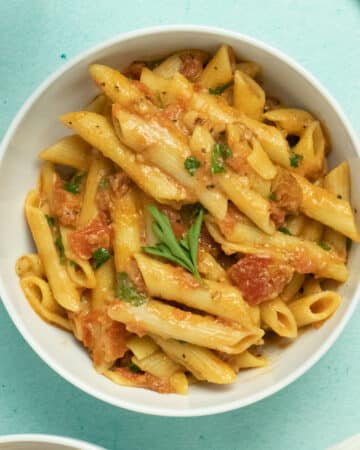 A bowl of penne sits on a blue table