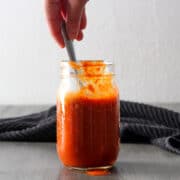 hand spooning hot sauce out of a jar