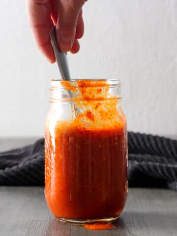 hand spooning hot sauce out of a jar