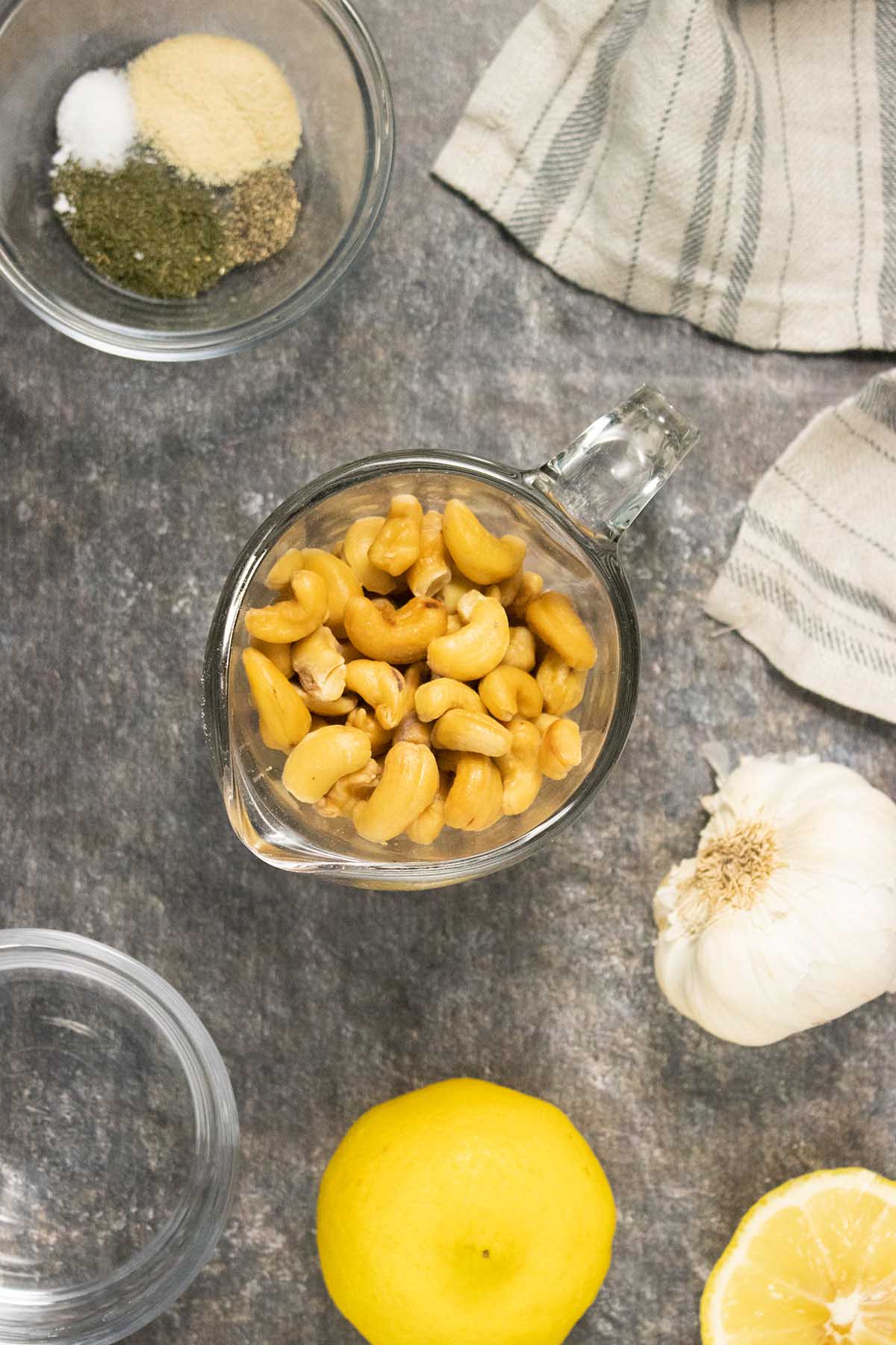 soaked cashews on a table with spices, lemon, and garlic