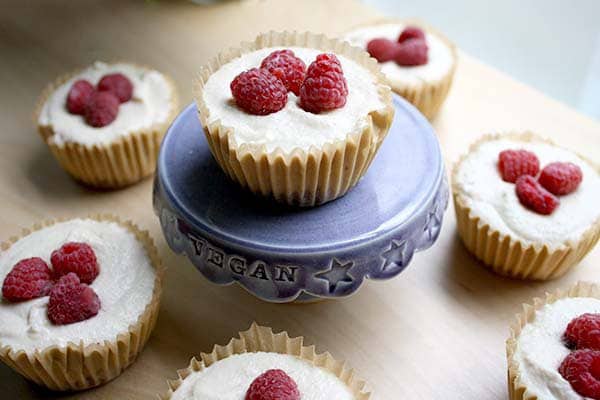 mini vegan cheesecakes topped with raspberries on a serving tray 