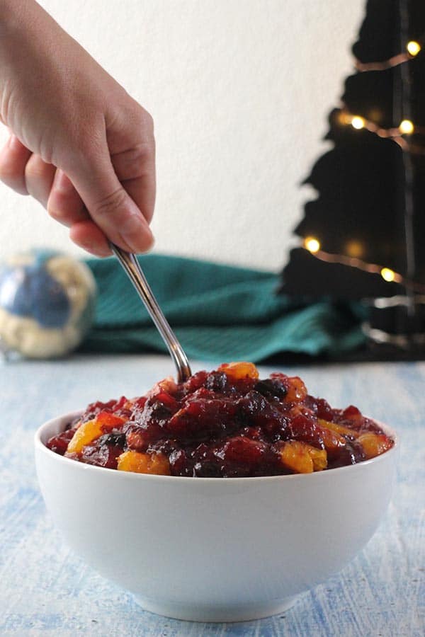 person dipping a spoon into a bowl of orange cranberry sauce
