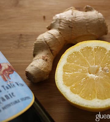 a bottle of wine next to lemon and ginger on a cutting board