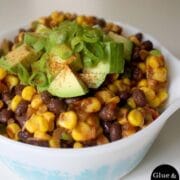 close-up of corn and bean salad with chopped avocado and green onion in a bowl