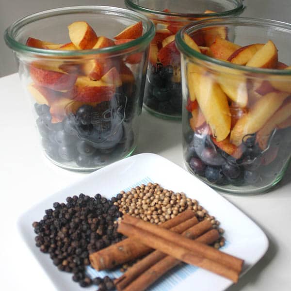 jars of peaches and blueberries, ready to pickle, next to a tray of black peppercorns, coriander seeds, and cinnamon sticks