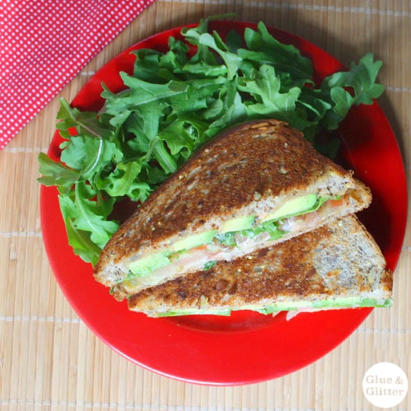 vegan grilled avocado sandwich on a plate next to an arugula salad