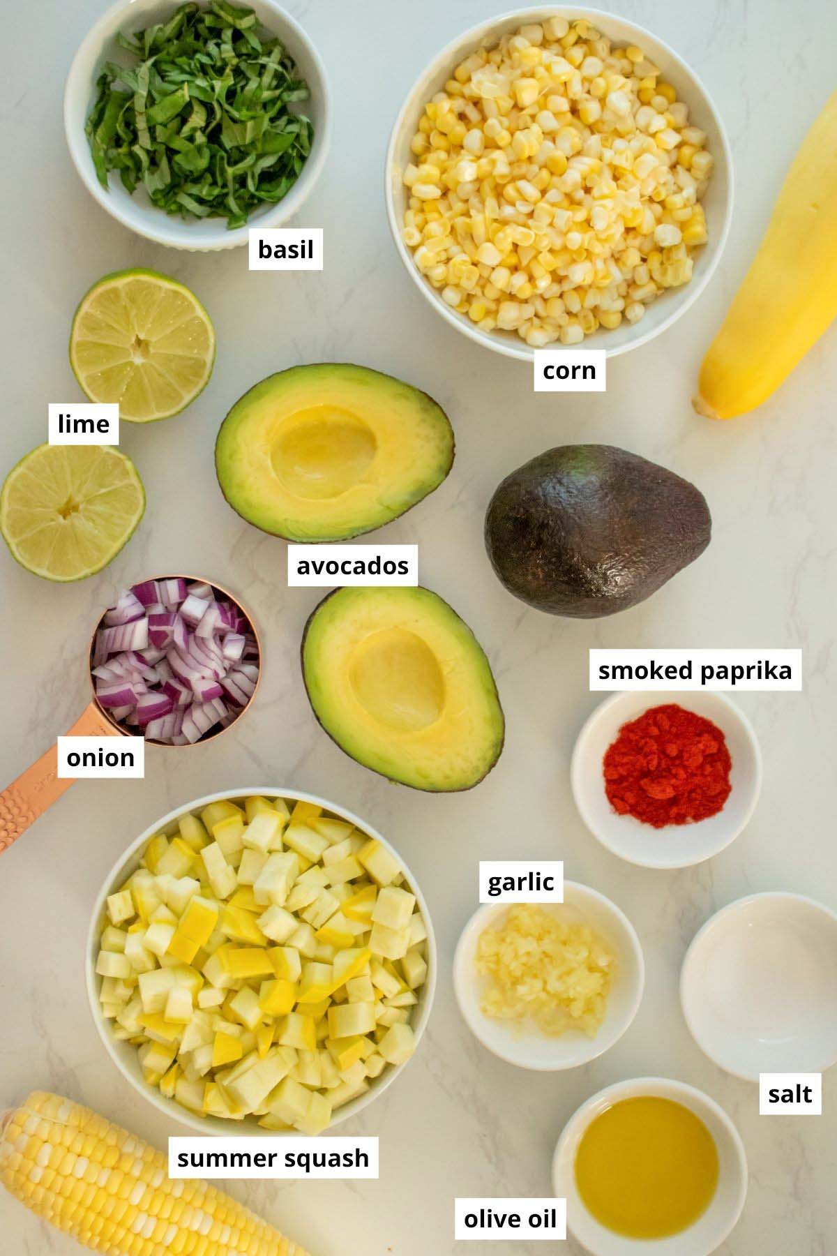 avocados, corn, squash, and seasonings in bowls on a white table