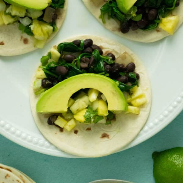 plate of spinach tacos with black beans, pineapple salsa, and sliced avocado