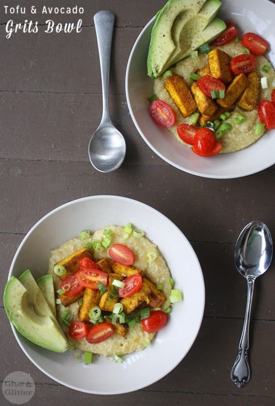 overhead photo of a grits bowl with tofu, tomato, green onion, and avocado slices on a wooden table