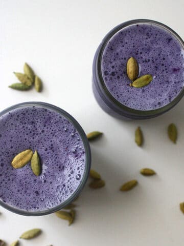 overhead photo of blueberry smoothies in a glass with cardamom pods for garnish