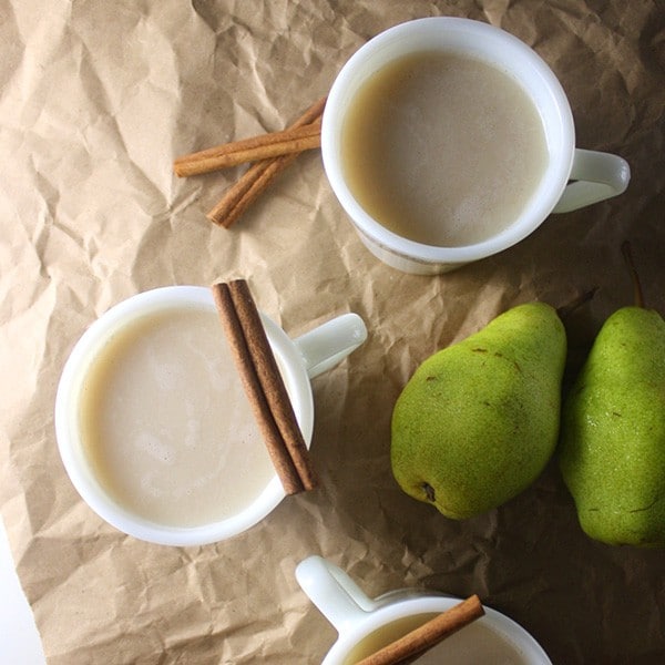 overhead photo of roasted pear vegan buttered rum in mugs with cinnamon stick garnish and pears on the table