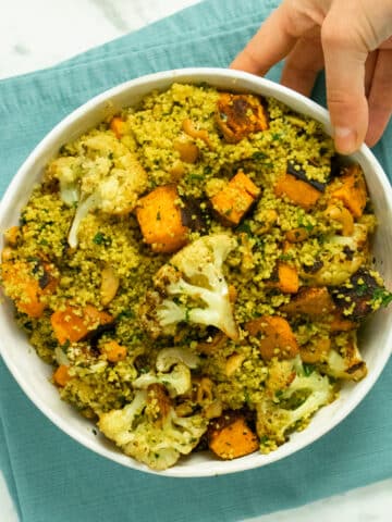 hand placing a bowl of curried couscous salad with roasted vegetables on a table
