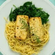 close-up of lemon herb tofu on a white plate served over a bed of spaghetti and spinach
