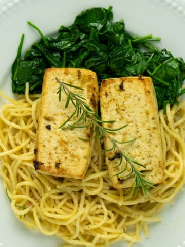 close-up of lemon herb tofu on a white plate served over a bed of spaghetti and spinach