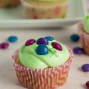 A close up of a cupcake with light green frosting topped with vegan M&M-style candy