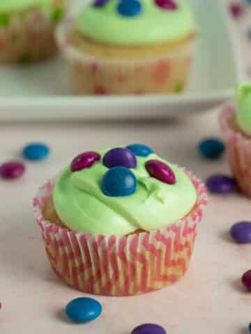 A close up of a cupcake with light green frosting topped with vegan M&M-style candy