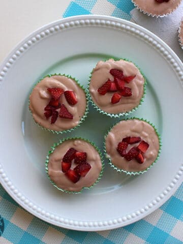 white serving plate of miniature vegan strawberry cheesecakes garnished with sliced strawberries