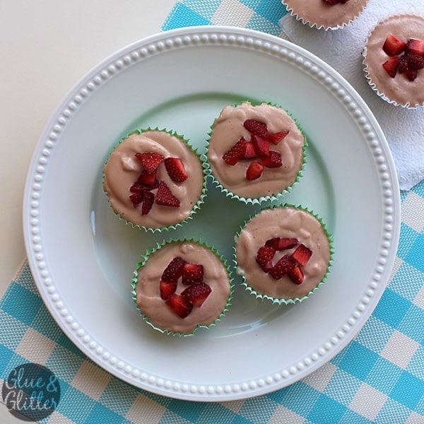 white serving plate of miniature vegan strawberry cheesecakes garnished with sliced strawberries