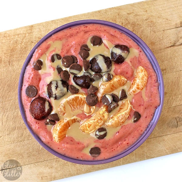 overhead photo of a cherry orange smoothie bowl topped with tangerine pieces, cherries, chocolate chips, and a tahini drizzle