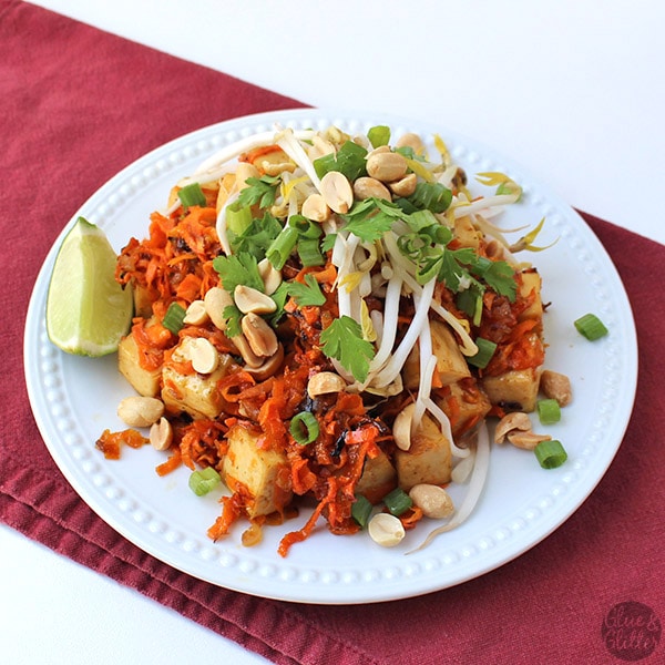 orange tofu over sweet potato noodles with peanuts, green onion, and bean sprouts, lime wedge on the side