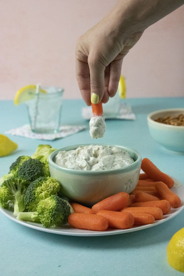 dipping a carrot into ranch party dip so you can see how thick and creamy it is