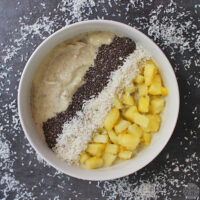 overhead photo of pineapple coconut smoothie bowl garnished with chia seeds, shredded coconut, and pineapple