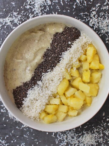 overhead photo of pineapple coconut smoothie bowl garnished with chia seeds, shredded coconut, and pineapple