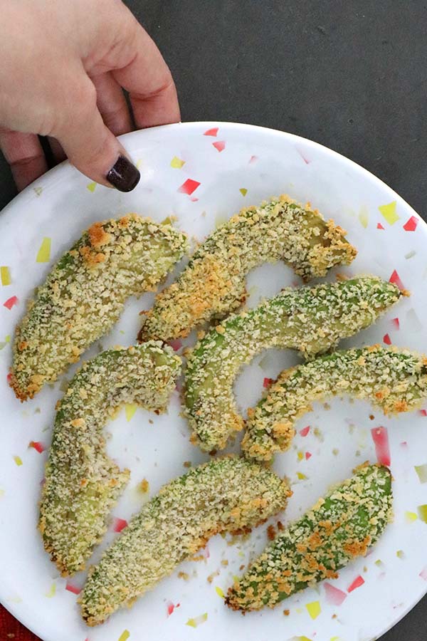 hand holding a plate of avocado fries