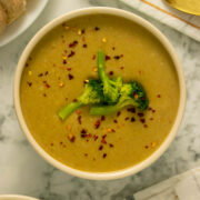 bowl of creamy vegan broccoli soup topped with steamed broccoli and red pepper flakes