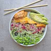 overhead photo of a spicy sushi bowl with edamame, vegetables, sesame seeds, mango, and avocado