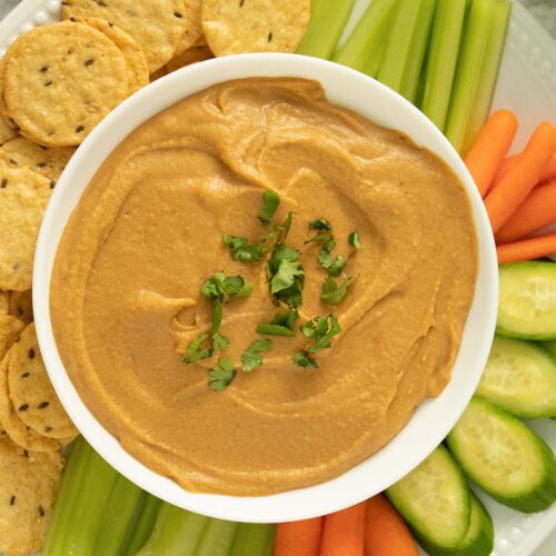 BBQ hummus in a white bowl surrounded by crackers and veggies