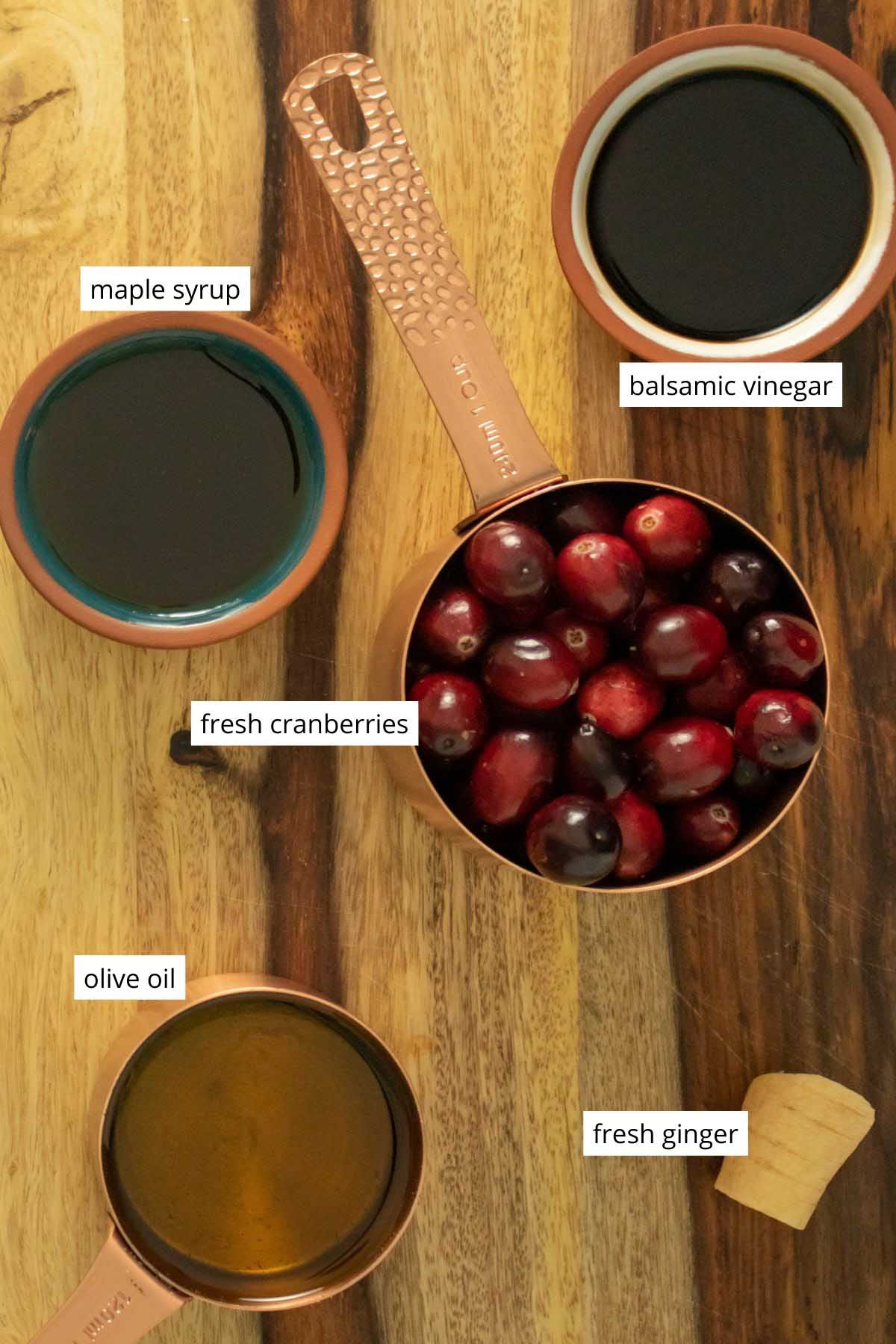 cranberries and other vinaigrette ingredients in small bowls on a wooden cutting board, text labels on each ingredient