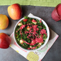 overhead photo of holiday kale salad with apples and a swirl of hot pink cranberry dressing