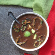 bowl of pureed tomato black bean soup with crispy peppers and avocado garnish, spoon sits in the bowl