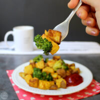 A person holding a fork with a bite of tofu, potato, and broccoli