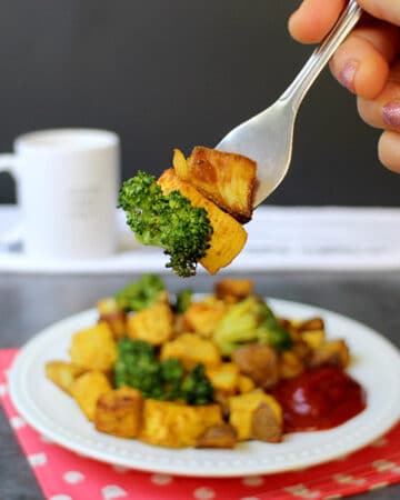 A person holding a fork with a bite of tofu, potato, and broccoli