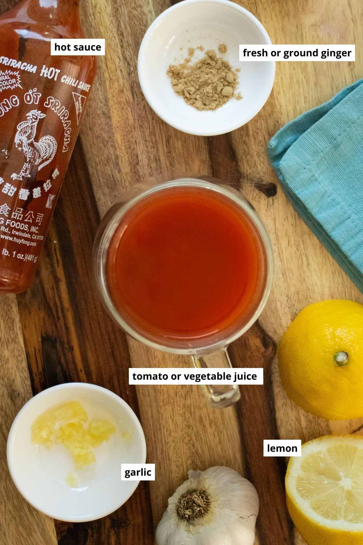 hot sauce, ginger, lemon, garlic, and tomato juice in cups and bottles on a wooden countertop