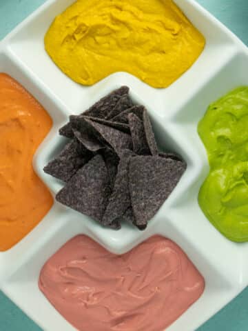 serving platter of 4 colors of hummus with blue corn chips in the center