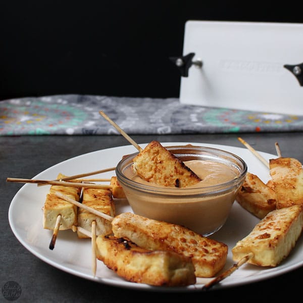 tofu satay on a serving platter with one skewer dipped into the peanut dressing