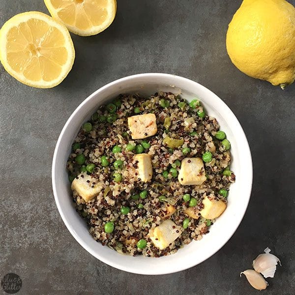 bowl of quinoa with peas and tofu next to garlic cloves and lemons