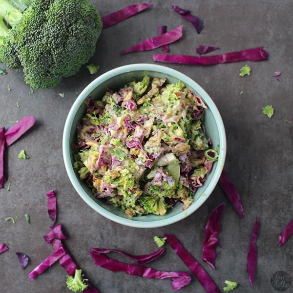 overhead photo of broccoli slaw in a bowl with purple cabbage and broccoli on the table