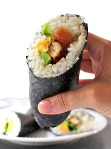 hand holding a vegan sushi burrito with tofu, avocado, mango, and pickled ginger