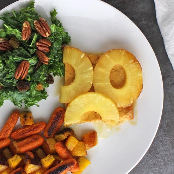 overhead close-up of pineapple glazed tofu on a white plate next to roasted vegetables and kale salad