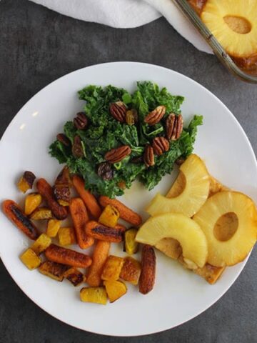 overhead photo of pineapple glazed tofu on a white plate next to roasted vegetables and kale salad
