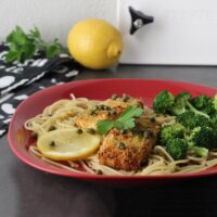 tofu piccata over spaghetti on a plate with lemon rounds and steamed broccoli