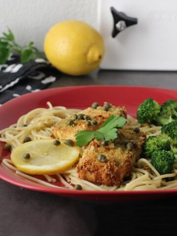tofu piccata over spaghetti on a plate with lemon rounds and steamed broccoli