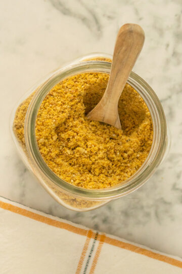 glass jar of vegan parmesan cheese with a wooden scoop in it