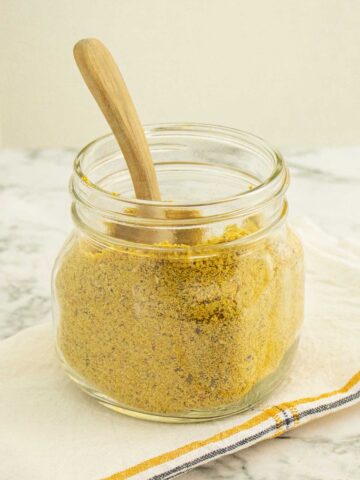 glass jar of vegan parmesan cheese with a wooden scoop in it