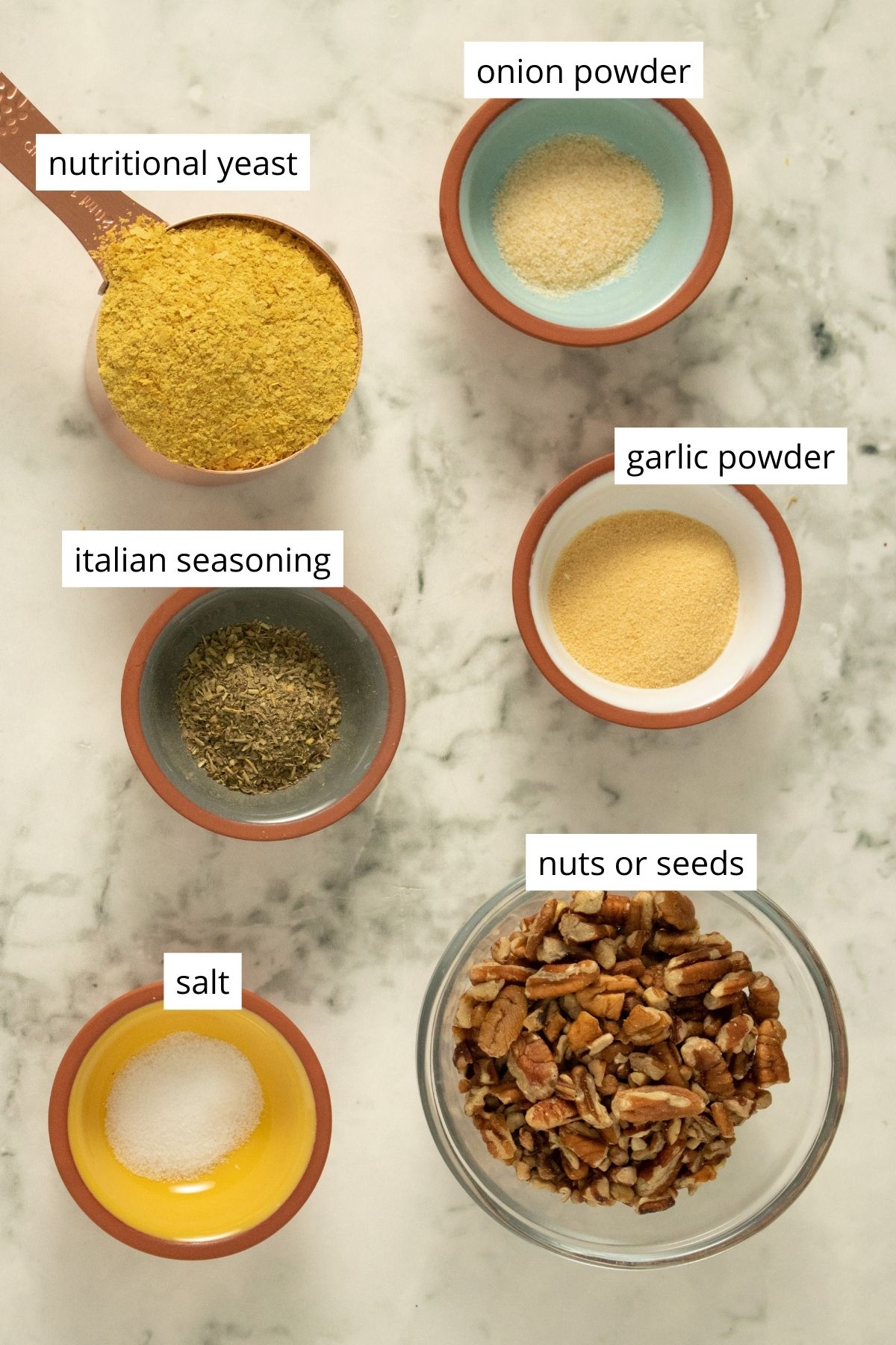 nutritional yeast, nuts, and spices in bowls on a marble table