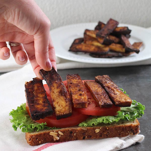 hand placing a piece of tofu bacon onto a vegan BLT